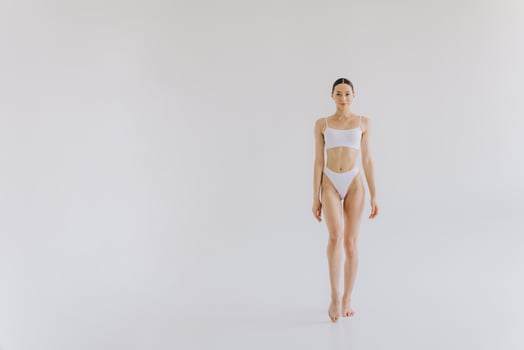 Full-length portrait of beautiful woman with slim body in underwear posing in the white studio background with copy space, mock-up photo