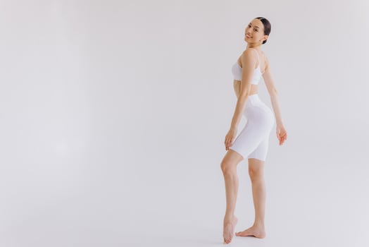 Slim woman in white sportwear on white background isolated. Muscular slim attractive female with flat belly. Copy space for text. Body care, healthy and sporty life, hair removal, yoga concept photo