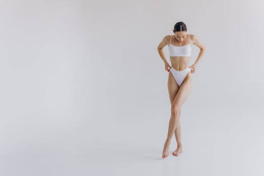 Full-length portrait of beautiful woman with slim body in underwear posing in the white studio background with copy space, mock-up photo