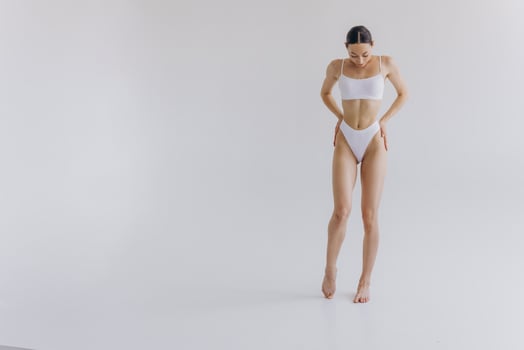 Full-length portrait of beautiful woman with slim body in underwear posing in the white studio background with copy space, mock-up photo
