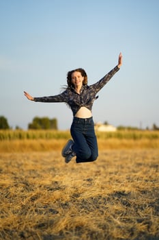 A Joyful Young Woman Happily Jumping in a Beautiful Golden Field Under the Sunlight photo