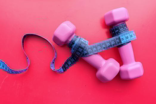 A pair of Pink Dumbbells and a Measuring Tape beautifully presented on a vibrant Red Background photo