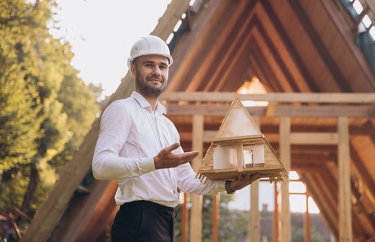 Man builder. Contractor for construction company. Architect in unfinished building. Builder in wooden modular house under construction. Male engineer holding a model of a miniature wooden house photo