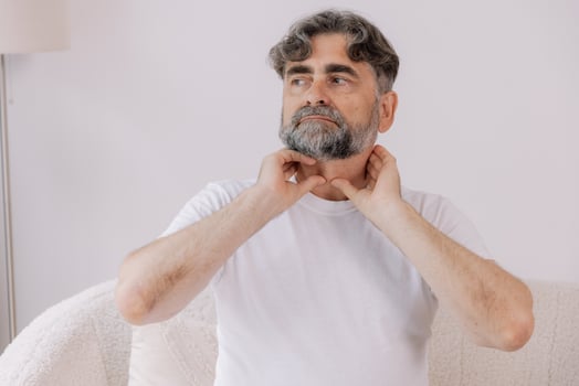 Gray-haired man has a severe sore throat, senior experienced male sitting on sofa holding his hand by the throat inflammation and sore throat. photo