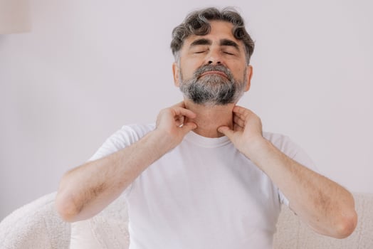 Gray-haired man has a severe sore throat, senior experienced male sitting on sofa holding his hand by the throat inflammation and sore throat. photo
