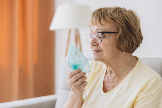 Sick senior woman has a viral infection or flu, labored breathing, asthma. An elderly female is using inhaler, nebulizer for self treatment sitting alone on the sofa at home photo