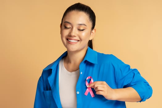 Asian woman smiling and showing pink ribbon pinned on shirt for breast cancer awareness photo