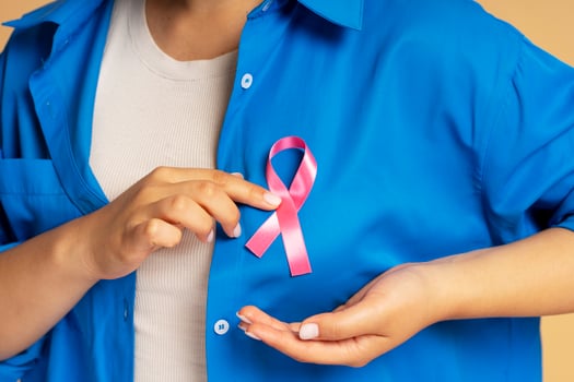 Woman attaching pink ribbon to her blouse showing support for breast cancer awareness photo