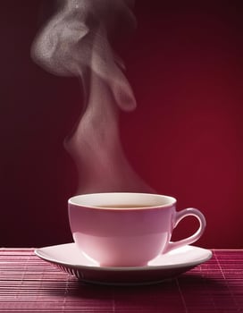 Tea cup with steam, on maroon background photo