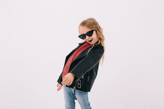 Funny little girl in a leather jacket and sunglasses listens to rock music and dancing photo