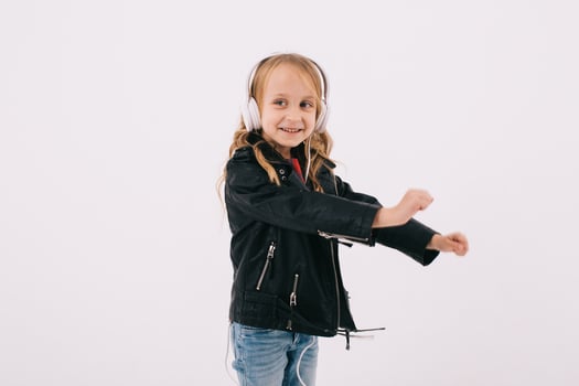 Funny little girl in a leather jacket listens to rock music in headphones and dancing photo