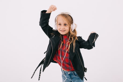 Funny little girl in a leather jacket listens to rock music in headphones and dancing photo