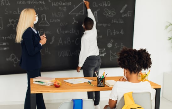 Female teacher teaches children at school near the blackboard. Quarantine, mask mode, covid-19. Back to school. photo