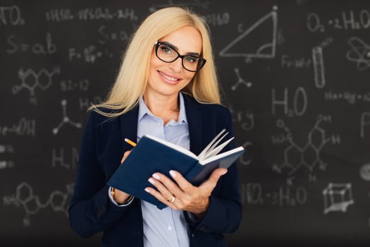 Portrait of happy blonde teacher woman standing near the blackboard in the classroom. photo