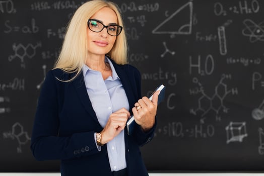 Portrait of happy blonde teacher woman standing near the blackboard in the classroom. photo