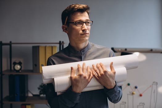 Attractive young man architect in glasses standing isolated over night office background, carrying drawings, holding house scheme photo
