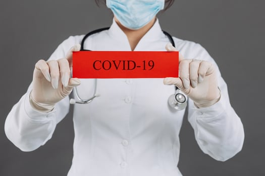 Doctor woman with surgical mask pointing to red paper with mesaage Coronavirus, isolated on gray background photo