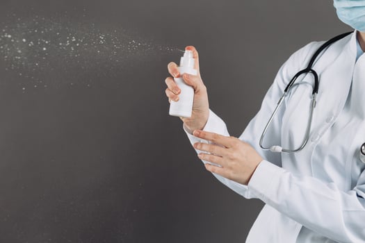 Doctor wearing surgical face mask holding showing alcohol spray pump bottle. Washing hands with alcohol spray or antibacterial soap sanitizer. Covid-19 or Coronavirus concept. photo