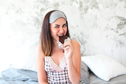 Cheerful young smiling woman in white shirt eating chocolate bar photo