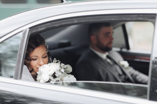 A bride and groom are in a car, with the bride holding a bouquet photo
