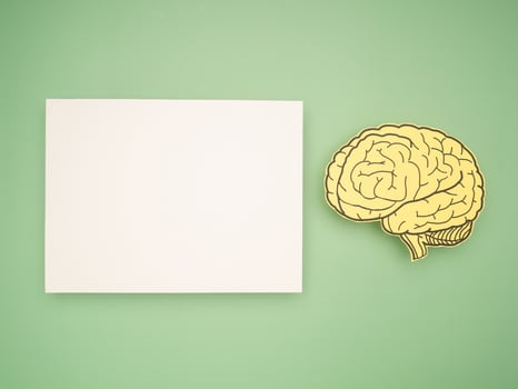 Blank white paper and a brain shape made from yellow paper on a gray background photo