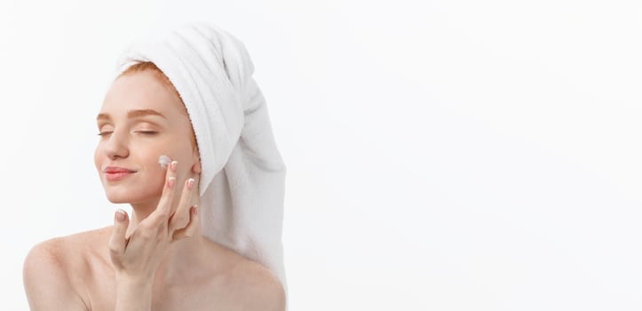 beautiful model applying cosmetic cream treatment on her face on white. photo