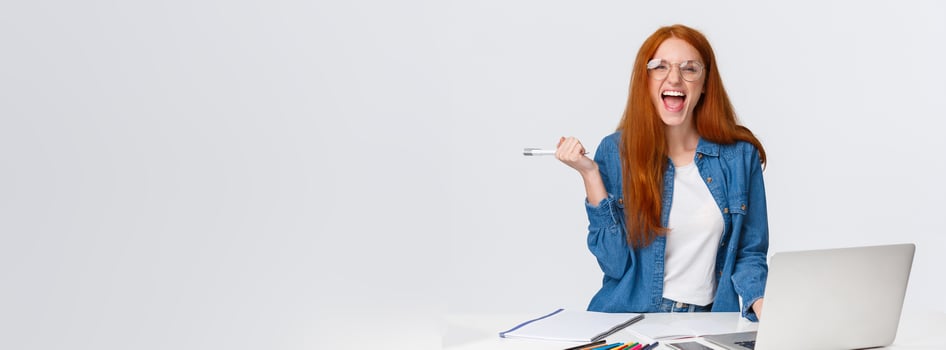 Excited and triumphing good-looking redhead female student passed challenge, found out final exam rating online using laptop, holding pen and screaming happily, standing white background photo