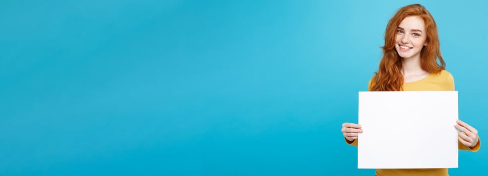 Business Concept -Close up Portrait young beautiful attractive ginger red hair girl smiling showing blank sign. Blue Pastel Background. Copy space. photo