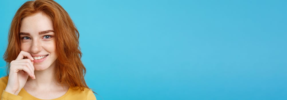 Headshot Portrait of happy ginger red hair girl with freckles smiling looking at camera. Pastel blue background. Copy Space. photo