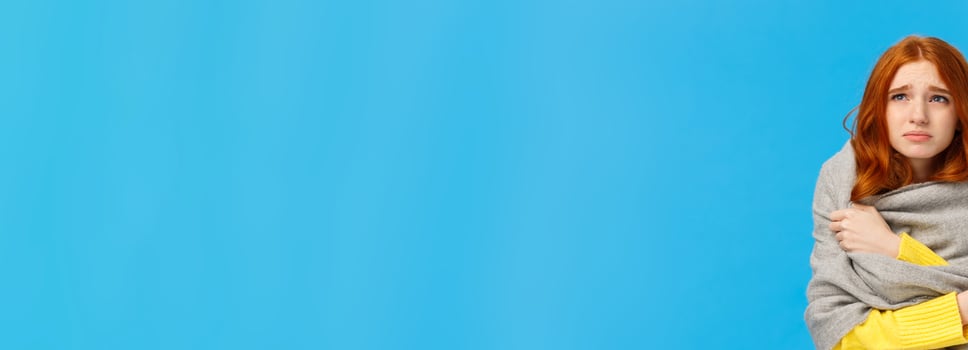 Girl sitting dormitory with broken heater, wrapping herself with warm scarf, looking upset and unwell upper left corner, grimacing suffer discomfort low temprature, catching cold, blue background photo