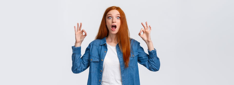 Amused, excited and thrilled good-looking redhead female in denim shirt, open mouth, drop jaw speechless staring with popped eyes camera, showing okay gesture in approval, white background photo