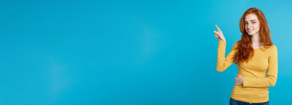 Close up Portrait young beautiful attractive redhair girl happy with something and pointing finger. Blue Pastel Background. Copy space. photo