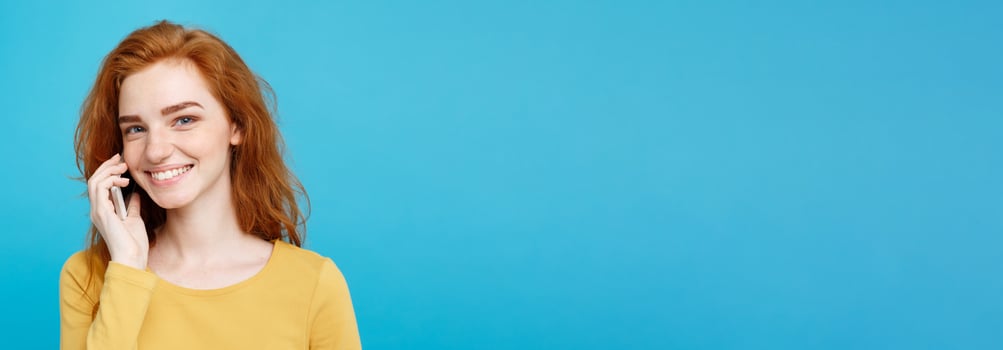 Lifestyle and Technology concept - Portrait of cheerful happy ginger red hair girl with joyful and exciting talking with friend by mobile phone. Isolated on Blue Pastel Background. Copy space. photo