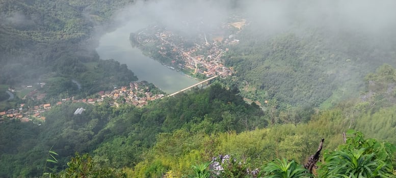 Aerial view of a foggy valley with a river, surrounded by lush green mountains and a small village. photo