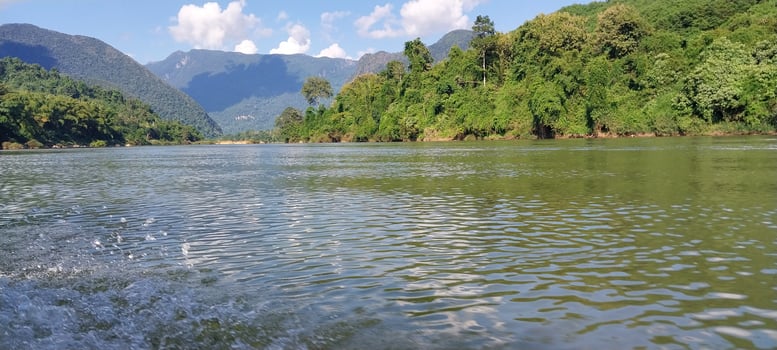 Scenic river view with lush green forests and mountains under a bright blue sky, showcasing natural beauty and tranquility. photo