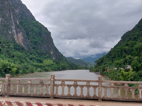 Scenic view of a river winding through lush green mountains under a cloudy sky, seen from a bridge with a railing. photo