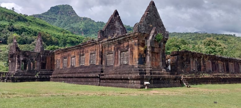 Ancient stone temple with intricate carvings, surrounded by lush greenery and mountains under a cloudy sky, a historical landmark. photo