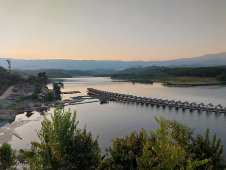 Scenic view of a reservoir with a bridge framed by lush greenery and mountains under a setting sun, capturing serene nature's beauty. photo
