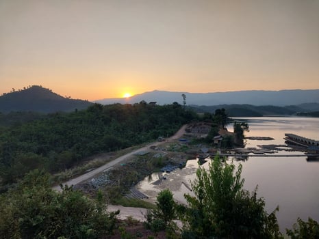 Scenic sunrise over a tranquil lake surrounded by lush greenery and distant mountains, capturing nature's serene beauty and peaceful ambiance. photo