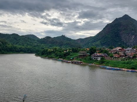 Scenic riverside village nestled in lush green mountains with cloudy skies, tranquil waters, and picturesque landscapes creating a peaceful atmosphere. photo