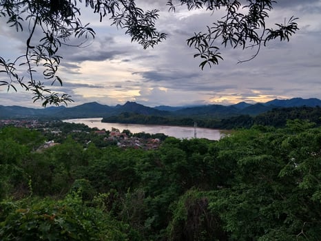 Scenic view of lush green forest and tranquil river under a cloudy sky, framed by foliage. Perfect for nature and landscape themes. photo