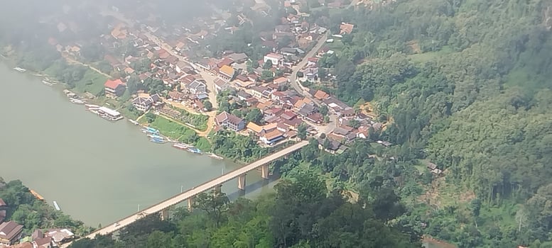Aerial view of a small town with a bridge over a river, surrounded by lush green hills and misty atmosphere. photo