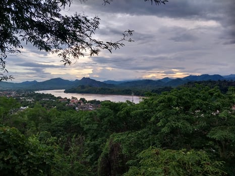 Scenic view of a lush green landscape with a river winding through the valley under a cloudy sky, surrounded by mountains at sunset. photo