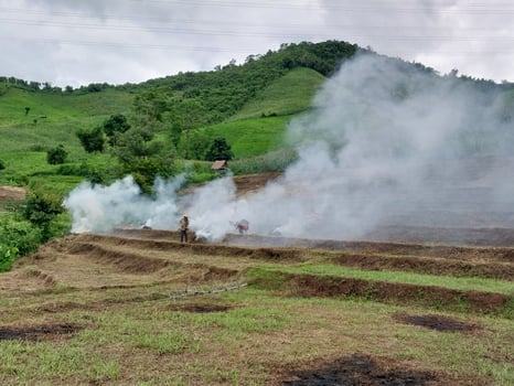 A vibrant landscape with hills and fields, featuring smoke rising in the foreground, hinting at a controlled burn or natural phenomenon. photo