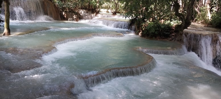 Tranquil stream flowing over multiple tiers of rock formations in a lush forest setting, creating a serene natural waterfall landscape. photo