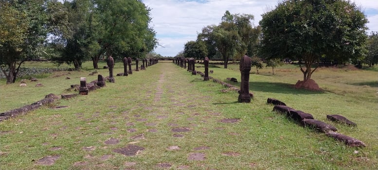 Ancient stone pathway aligned with weathered stone pillars and lush green trees under a partly cloudy sky. photo