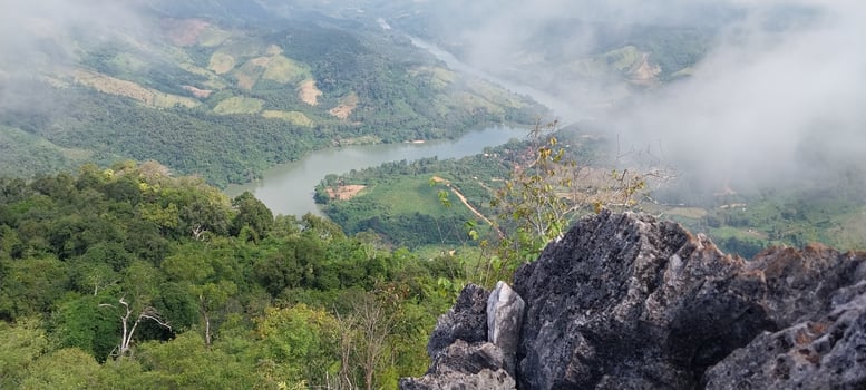 Scenic mountain landscape with lush greenery, river winding through the valley, and misty clouds above captured from a rocky peak. photo