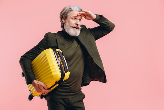 Bearded gray-haired middle-aged man in a suit hold a yellow suitcase on a pink background photo