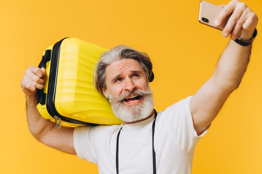 Stylish bearded and mustachioed man smiling and taking a selfie on his smartphone with a yellow suitcase. photo