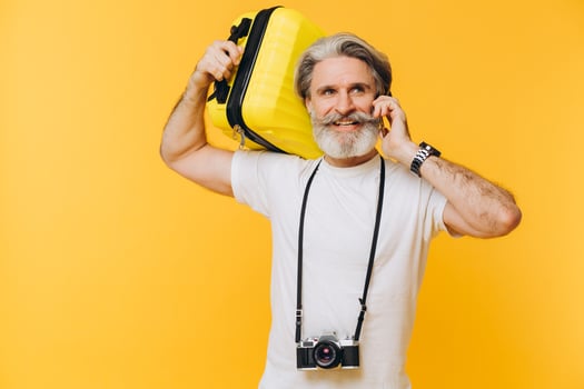 Stylish bearded man with camera laughing while holding a yellow suitcase chatting on the phone photo